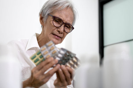 Asian senior woman is stressed about having to take a lot of medicine,medication to treatment,elderly hold medicine pills or capsules feeling bored of facial expressions,old people is tired of illnessの写真素材