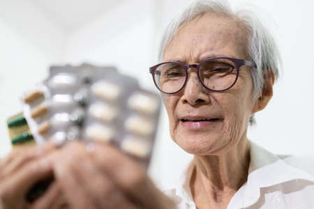 Sick senior woman holding medicine pills or capsules,sad female elderly showing a lot of drugs,treatment,medication to reduce pain,bored,afraid of taking medicine,asian old people is tired of illnessの写真素材