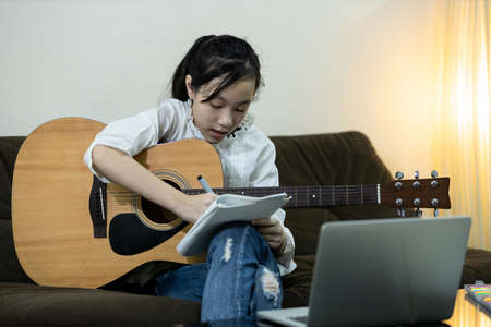 Happy asian teen girl is practicing composing a song,trying to write a new music in her diary,female people relaxing time,hobby,lifestyle,inspiration,creative musician enjoy write making up a lyricsの写真素材