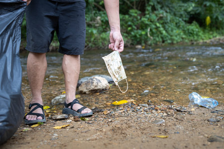 Hands of volunteer is picking up trash,rubbish of face mask with garbage bag on the streams of...