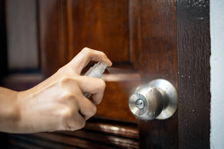 Hand of woman is spraying alcohol,disinfecting door knob with disinfectant spray at public...