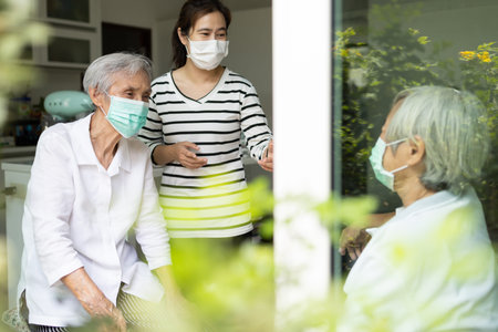 Asian woman and old elderly with medical masks on the face,daughter talking happily visited her...