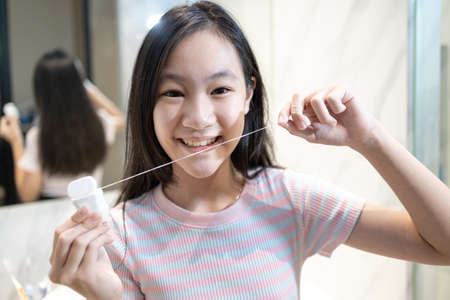Happy smiling asian student girl flossing her teeth,clean her healthy teeth in the morning,beautiful woman brushing with dental floss in the bathroom, teeth care,oral hygiene,dental health conceptの写真素材