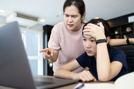 Angry mother scolding her daughter about an education on computer,stressed student suffers from displeasure of female tutor or teacher,sad disappointed child girl receives reprimand rebuke incompetentの写真素材