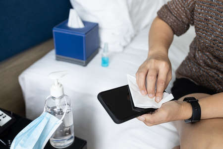 Hands of asian people using tissue paper with alcohol to wipe clean the phone,wipe after spraying alcohol to disinfect on mobile phone,safety from Coronavirus,new normal life condition under COVID-19の写真素材