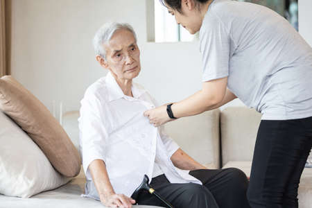 Asian granddaughter taking care of helping senior grandmother get dress,button up shirt for the elderly Alzheimer's,chang clothes to prepare to travel,holiday and summer vacations,lifestyle conceptの写真素材