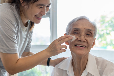 Female caregiver assisting to apply sunscreen lotion on the face of senior woman,granddaughter using...