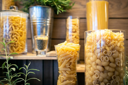 Variety of raw pasta penne,fusilli,macaroni,spaghetti,shapes of pasta in glass jars on a wooden table,Pasta pieces in the form of short hollow fluted tubes,short spirals,Italian cuisine food conceptの写真素材