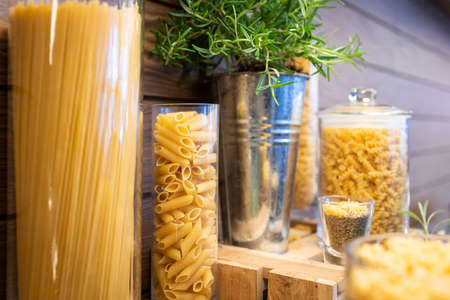 Variety of raw dry pasta in glass jars on a wooden tableの写真素材