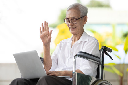 Happy smiling asian senior woman using laptop computer,old elderly making distance video call,greeting,say hi,wave her hand,talk chat online meeting to relatives her family or friends,stay at homeの写真素材