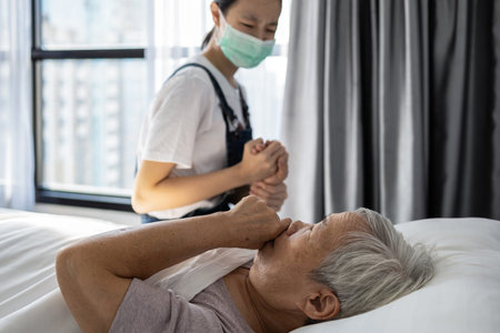 Old elderly patient lying on the bed holding hand of granddaughter,asian child girl wearing...