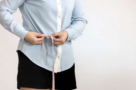 Close up,belly of female,asian young woman hold tape measure check waistline,healthy girl measuring around waist size with tape,waist measurement for fat checking,health care,weight control conceptの写真素材