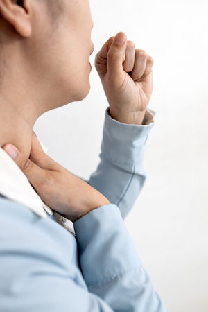 Sick asian woman with coughing into her fist and puts hand to her painful neck,sore...