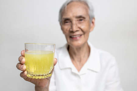 Healthy asian senior grandmother drinking a glass of vitamin C or orange juice,elderly people with effervescent vitamin C,strengthening the immunity for cold,flu,fightの写真素材