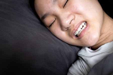 Asian child girl suffering from bruxism while lying in bed at night,female grinding of the teeth...