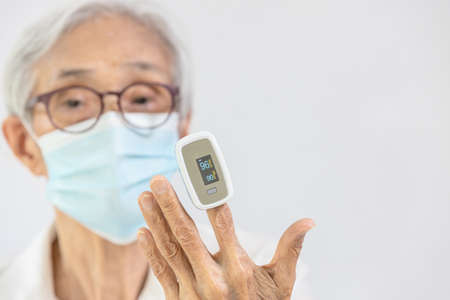 Hand of asian elderly woman with fingertip pulse oximeter on finger,old people measuring heart rate,pulse rate,checking oxygen saturation level in the blood,diagnosis of  virus at homeの写真素材