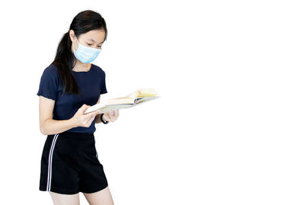 Young school girl standing holding book,student wearing protective mask reading a book during Coronavirus COVID-19 outbreak at library isolated on white background,Hygiene and Education conceptの写真素材