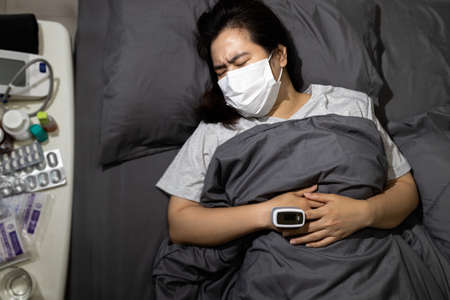 Sick female patient has a fever from virus infection,illness of ,resting in her bed with medicine and medical equipment,drugs to treat disease,home isolation quarantine,self-treatmentの写真素材