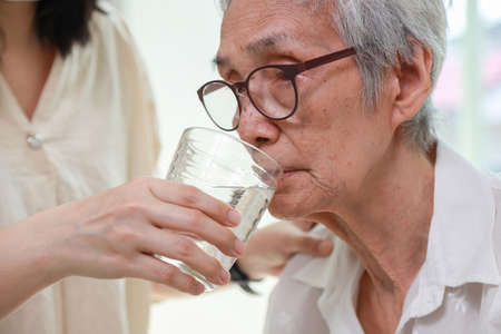 Nurse or caregiver gives drinking fresh water to senior woman in hospital or nursing home,Thirsty elderly grandmother suffering from heat,exhausted and dehydrated,health care,healthy lifestyle conceptの写真素材