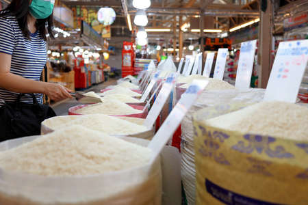 Female consumer buying grains of thai fragrant rice,choosing raw white rice,asian woman shopping in the market,purchasing or hoarding for dry food,rice prices problem,concept of nutrition,consumptionの写真素材