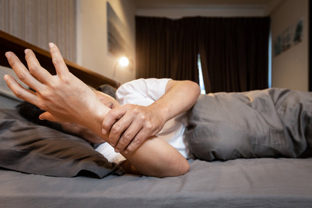 Sick asian middle-aged man with shaking of Parkinson's disease,symptom of resting tremor,stressed male patient holding his hand to control hands tremor while lying in bed,illness,health problemsの写真素材