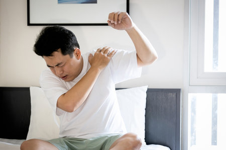 Asian middle aged man suffering from frozen shoulder,pain and stiffness,unable to move,difficulty lifting his arm,male people with calcific tendonitis or shoulder injuries,health care,medical conceptの写真素材