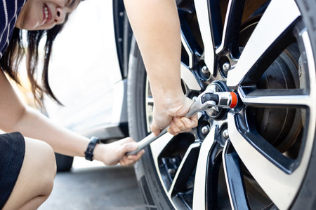 Tired woman with flat car tire,wrench in hands,trying to change wheel after a car breakdown,repairing with difficulty,accident with punctured tire while traveling,insurance and transportation conceptの写真素材