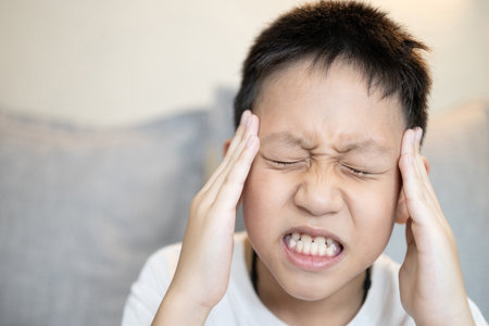 Sick child boy suffering from severe headache,holding his head,tension or migraine headache in children,pain in temple and head,illness,Increased Intracranial Pressure,disease of brain tumor or cancerの写真素材