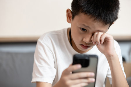Asian child boy overusing his smart phone,addicted to mobile phone,game addiction,effects on young children's brains,disease of ADHD,Nomophobia,dry eyes,eyesight problems,loss of vision,health careの写真素材