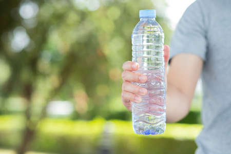 Hand holding water bottle in the parkの写真素材