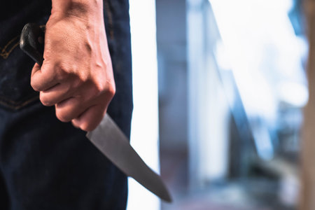 image of a robbers hands holding a knife in the shadows.