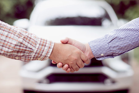 Close handshake Car dealer shakes hands with customers A man makes an agreement to buy a car in a car center. White cars placed in the backの写真素材