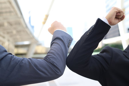 New greetings to avoid the spread of coronavirus, two male friends, businessmen, meeting on a downtown street, teeth elbows greet each other instead of bare hands. Instead of greeting them with a hugの写真素材