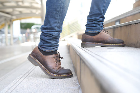 Close the legs of the shoes of a young businessman who steps up the stairs in a modern city, growing...