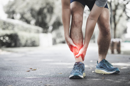 Man suffering from pain in the ankle while jogging in the parkの写真素材