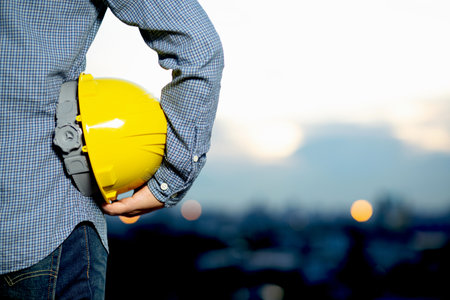 Closeup of a construction worker holding a yellow safety helmet on blurred backgroundの写真素材