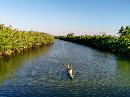 beautiful panorama with trees thriving on the banks of a clean river and on a small boat taking home a fishermanの写真素材