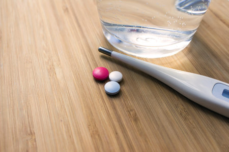 Thermometer, tablets and a glass of water on a wooden background, concept, self-isolation, treatment...