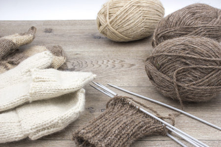 Skeins of thread and knitted mittens on a wooden background. The concept of hobby, home production...