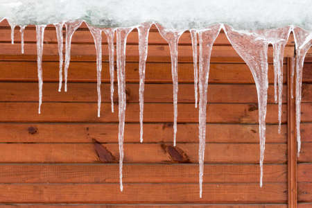 Icicles hang from the roof of a wooden house.の写真素材