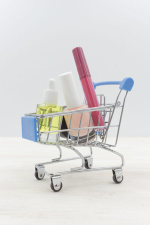 Cosmetics in the shopping cart on a white wooden table: lipstick, nail polish, cuticle oil, a jar of creamの写真素材