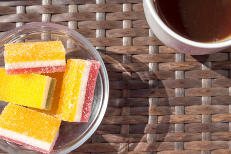 marmalade made of three layers sprinkled with granulated sugar in cubes in a glass plate and tea in...