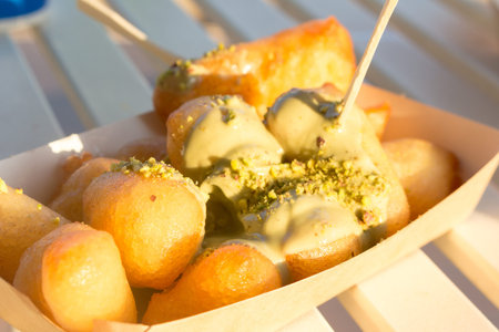 Greek lukumades donuts with pistachio-nut sauce sauce in a cardboard tray. street food, fast food.