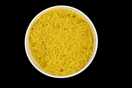 Uncooked dry vermicelli in white ceramic bowl, isolated on an black background, top view....
