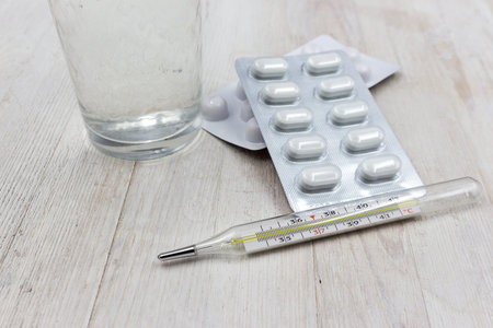 Thermometer, tablets and a glass of water on a wooden background, concept, treatment at home, save...
