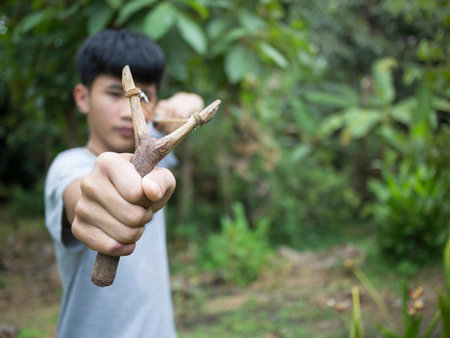 Portrait of the boy firing a rock from a slingshot in hands.