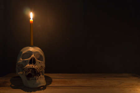 Human skull with candle light on wooden table in the dark background, Decorate for Halloween Theme with copy space.の写真素材
