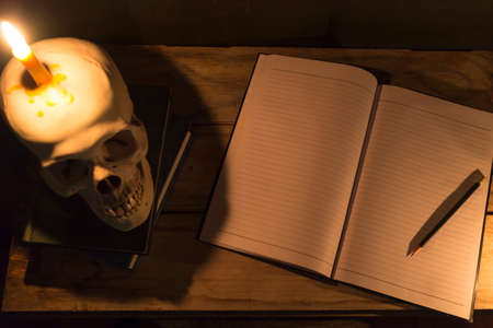 Human skull with candle light and notebook with pencil on wooden table, Decorated for Halloween Theme with copy space.の写真素材