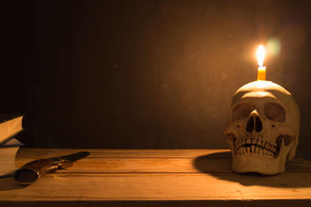 Human skull with candle light, Knife and book on wooden table in the dark background, Decorate for Halloween Theme with copy space.の写真素材