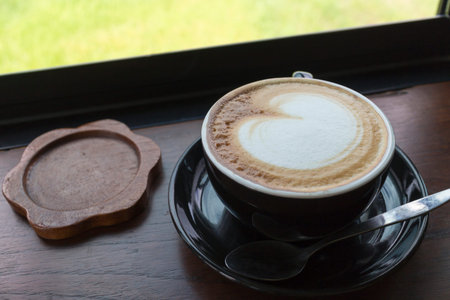 Black coffee cup with cappuccino on wooden table with glass window in a beautiful morning.の写真素材